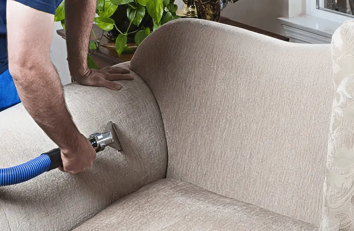 Professional upholstery cleaner deep-cleaning a fabric sofa with a handheld extraction tool and hose, Louisville, KY.